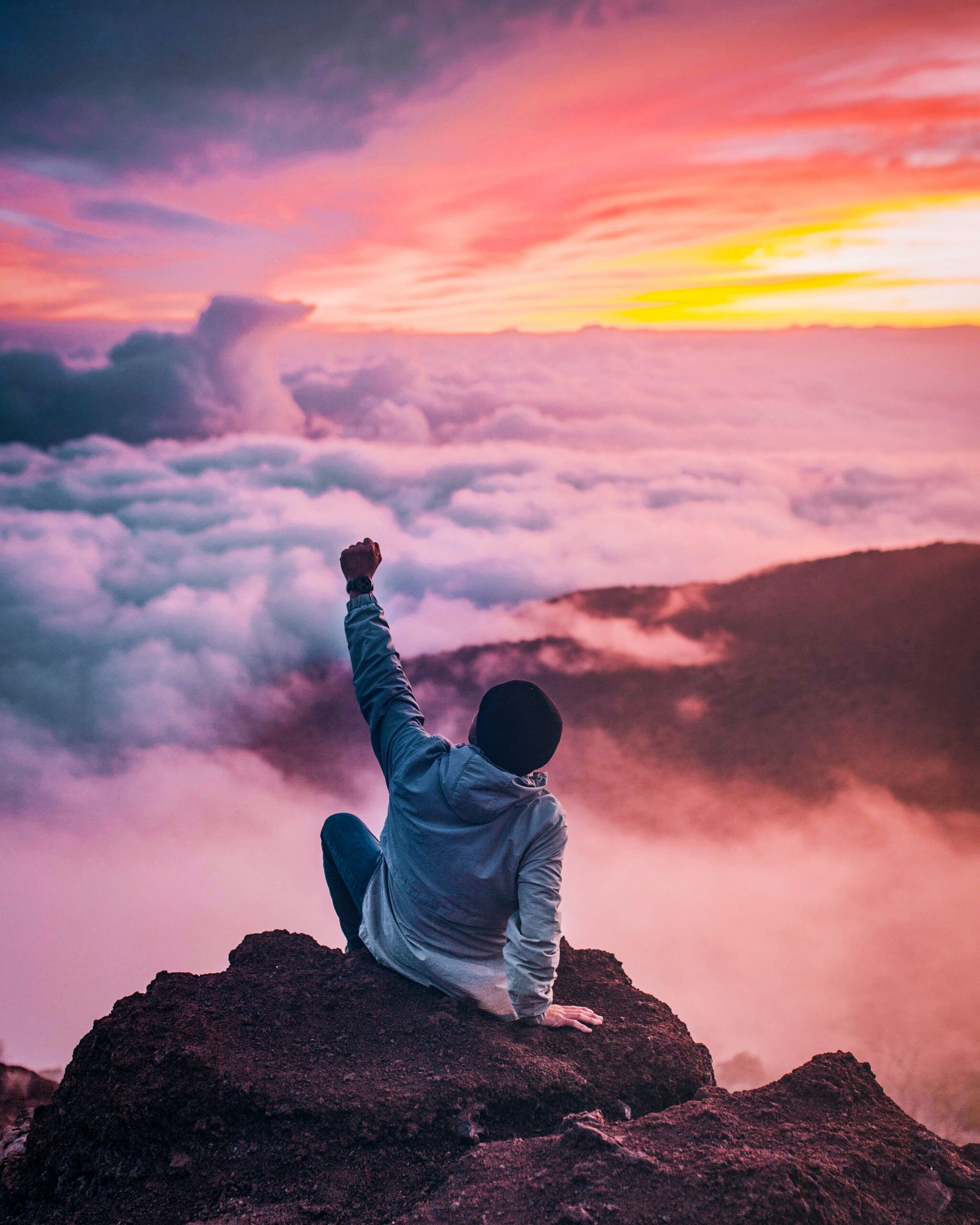person cheering on top of a mountain overlooking a sunset