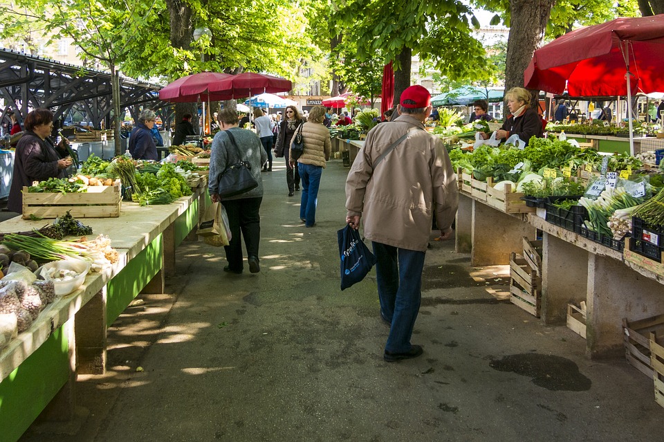 people at a farmers market with lots of vegetables. 